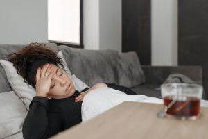 Woman lying on a couch appearing unwell, possibly experiencing a headache or ill