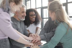 Side view of happy diverse multiracial coworkers uniting hands while standing ne