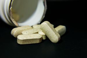 Close-up of white capsule pills spilled from a bottle on a black background. Ide