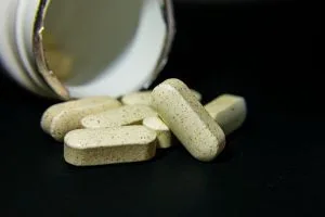 Close-up of white capsule pills spilled from a bottle on a black background. Ide