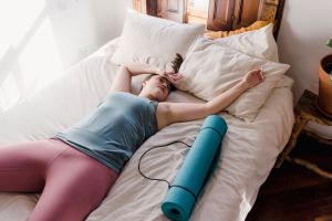 High angle of exhausted female in sportswear lying on bed with hands above head